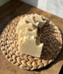 A bar of Oatmeal Vegan Hemp Milk Soap is partially sliced, revealing its creamy white interior with visible flakes of oats. The soap is placed on a woven mat