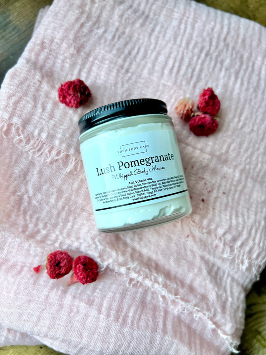 Eden Body Care Lush Pomegranate whipped body mousse jar displayed on soft blush fabric with dried red and pink flowers.