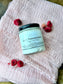 Eden Body Care Lush Pomegranate whipped body mousse jar displayed on soft blush fabric with dried red and pink flowers.