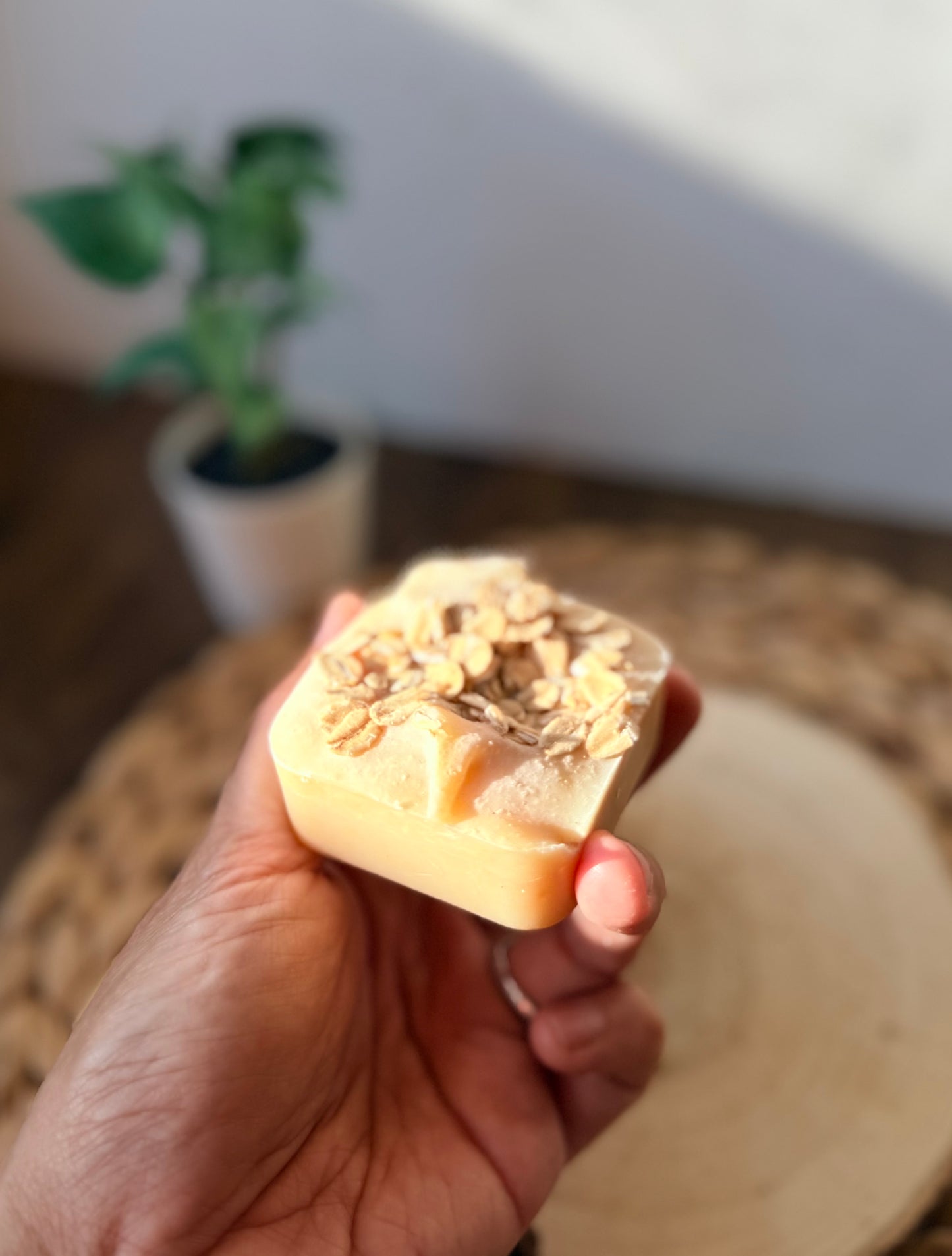 Close-up of a mini handmade oatmeal and honey soap bar topped with rolled oats and held in hand.