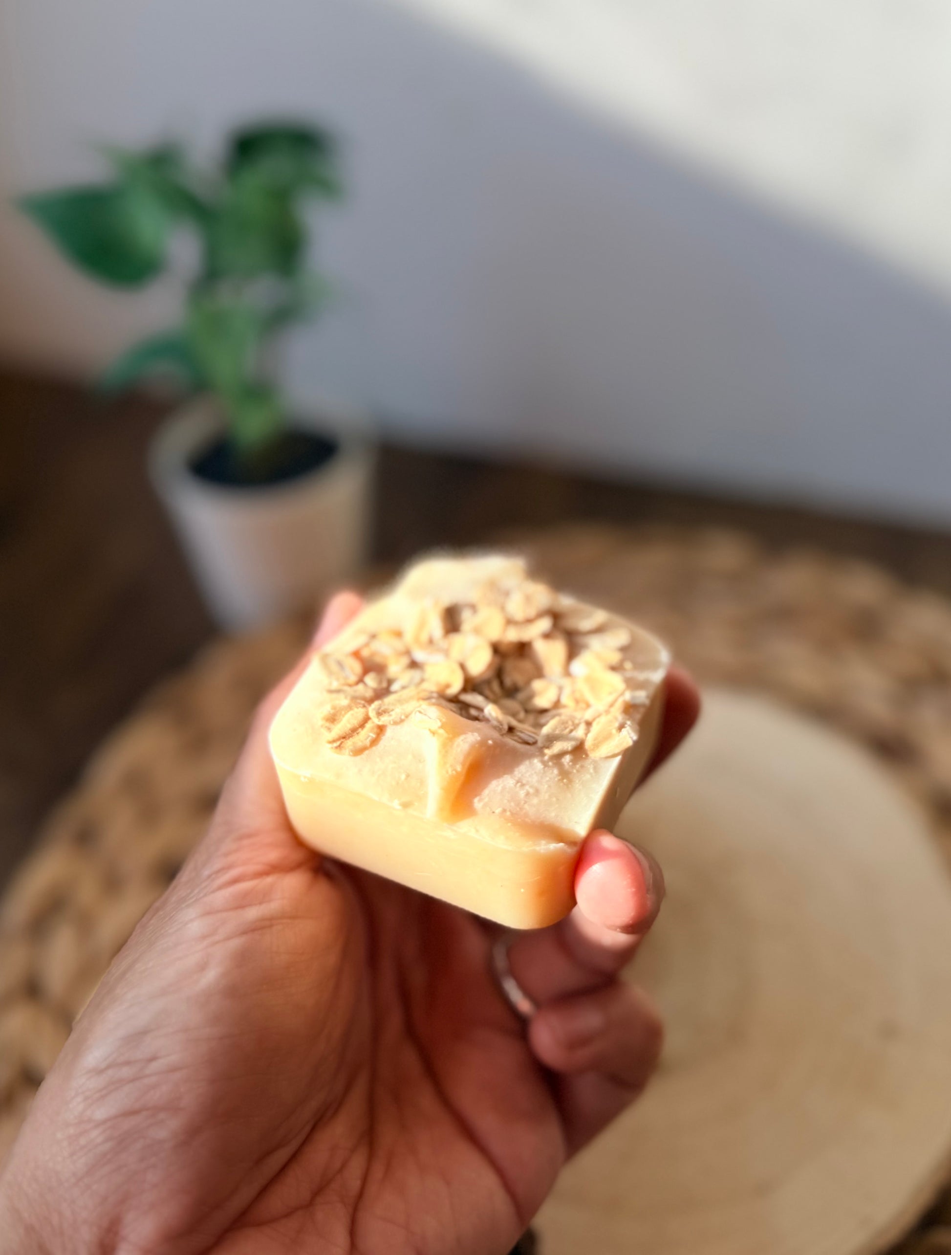 Close-up of a mini handmade oatmeal and honey soap bar topped with rolled oats and held in hand.