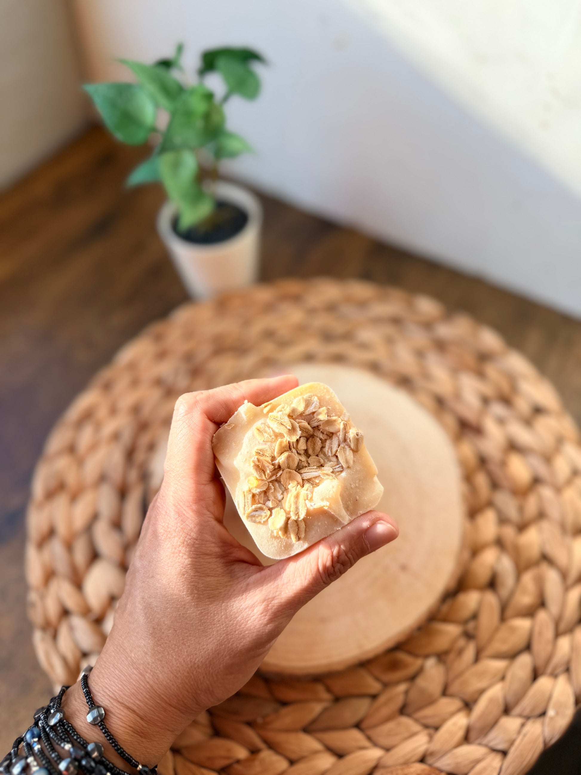 Mini handmade oatmeal and honey soap bar topped with rolled oats and held in hand to show its small giftable size.