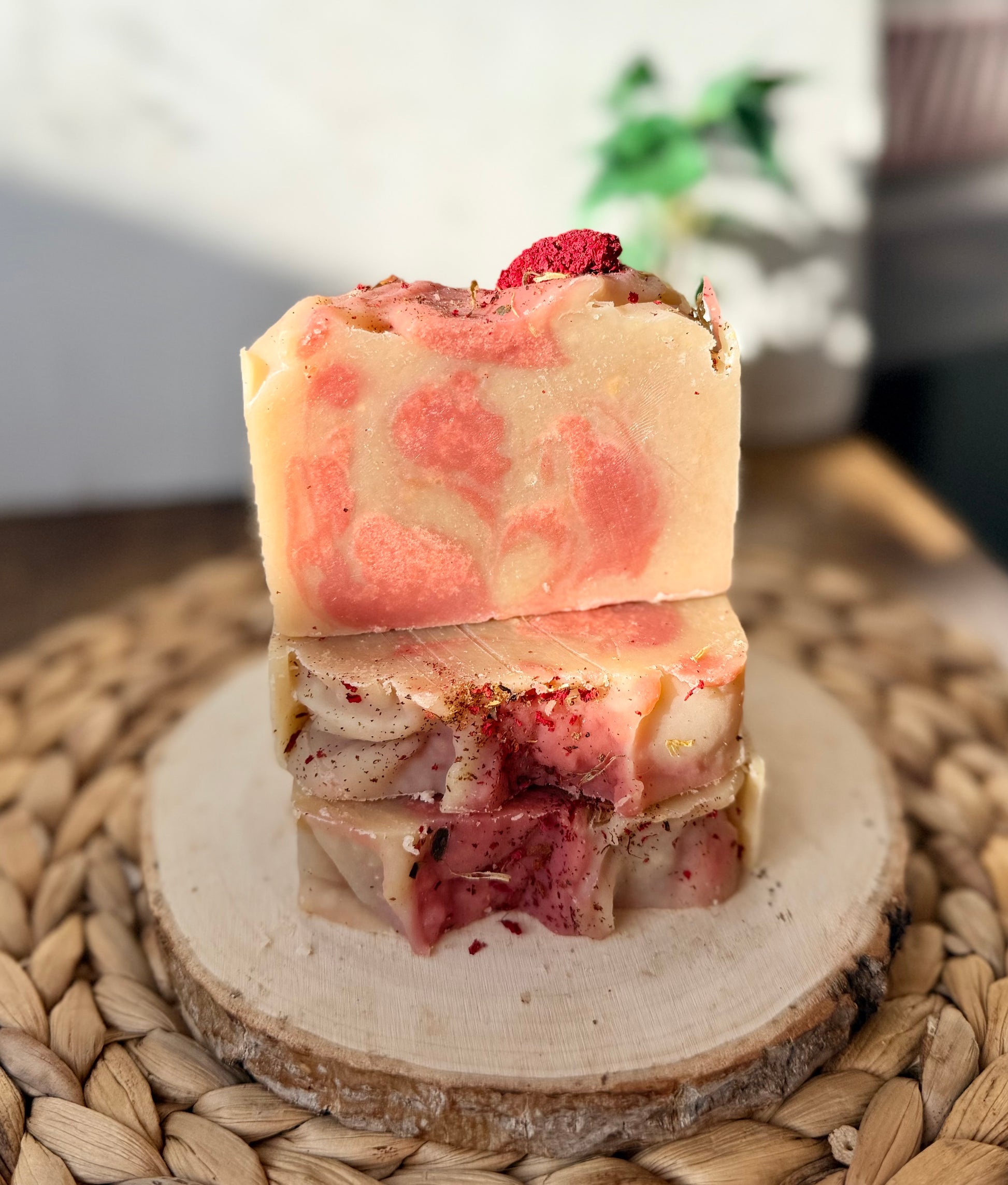 Eden Body Care Pomegranate Flowers handmade soap bars with pink and cream swirls, topped with dried floral accents and displayed on a natural wood slice.