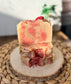 Eden Body Care Pomegranate Flowers handmade soap bars with pink and cream swirls, topped with dried floral accents and displayed on a natural wood slice.