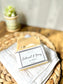 Stack of beige oatmeal and honey goat milk soap bars with oatmeal pieces on top, placed on a white wash cloth with a paper cigar band packaging.