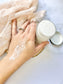 Open jar of Eden Body Care body mousse beside a hand showing the creamy whipped texture applied to the skin