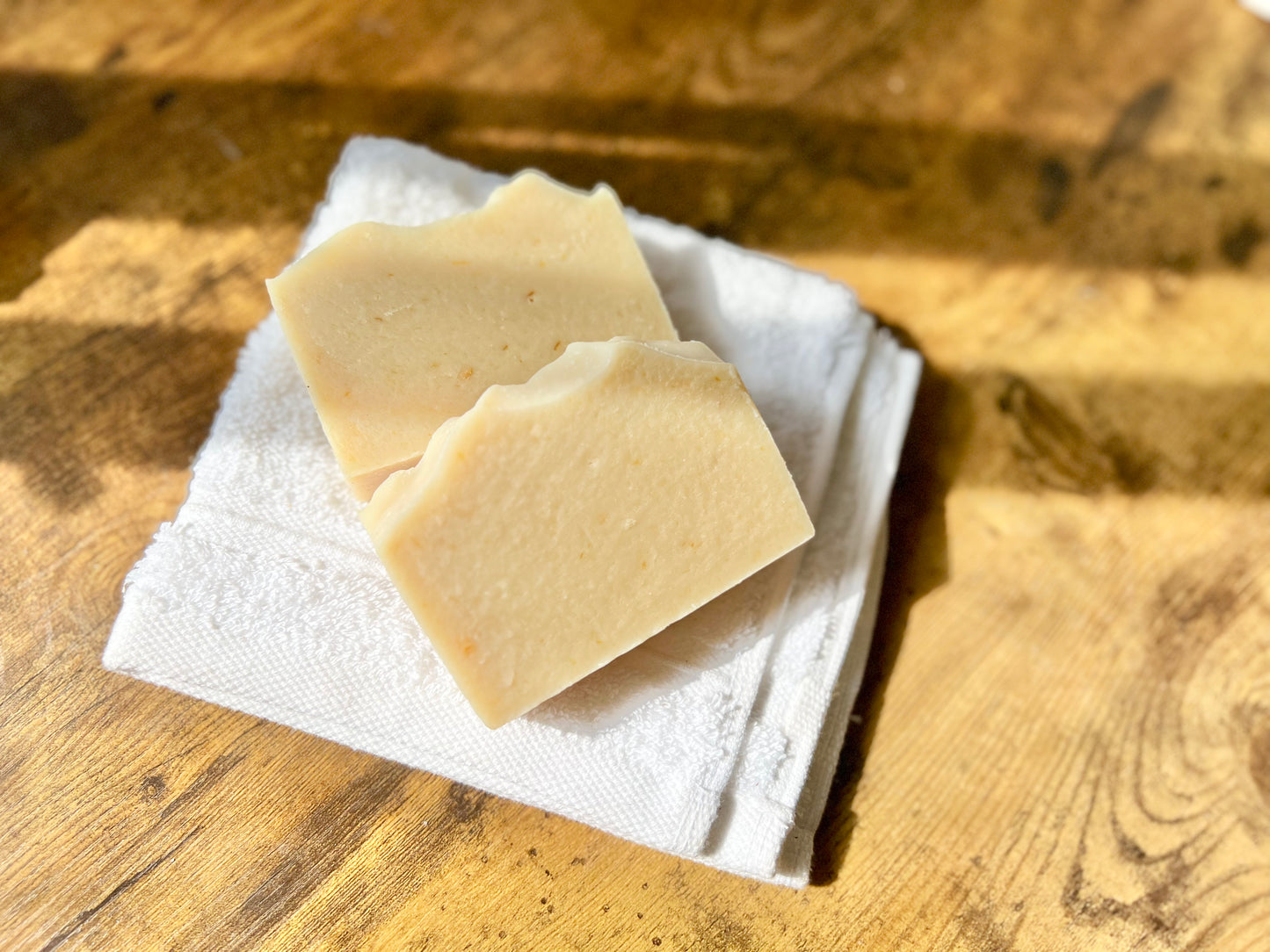 Two Eden Body Care Classic Unscented goat milk soap bars resting on a folded white towel in warm natural sunlight.