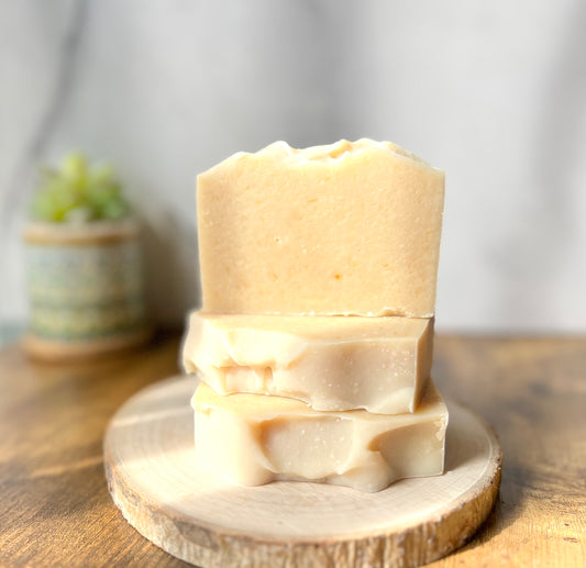 Eden Body Care Classic Unscented goat milk soap bars stacked on a natural wood slice in warm sunlight.