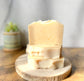 Eden Body Care Classic Unscented goat milk soap bars stacked on a natural wood slice in warm sunlight.