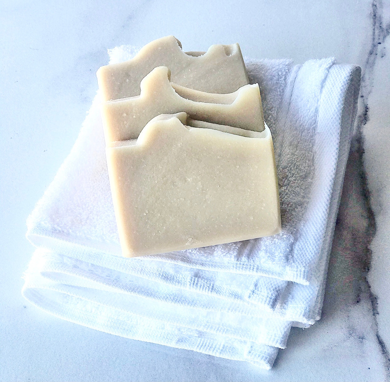 Three Eden Body Care Classic Unscented goat milk soap bars arranged on a folded white towel.