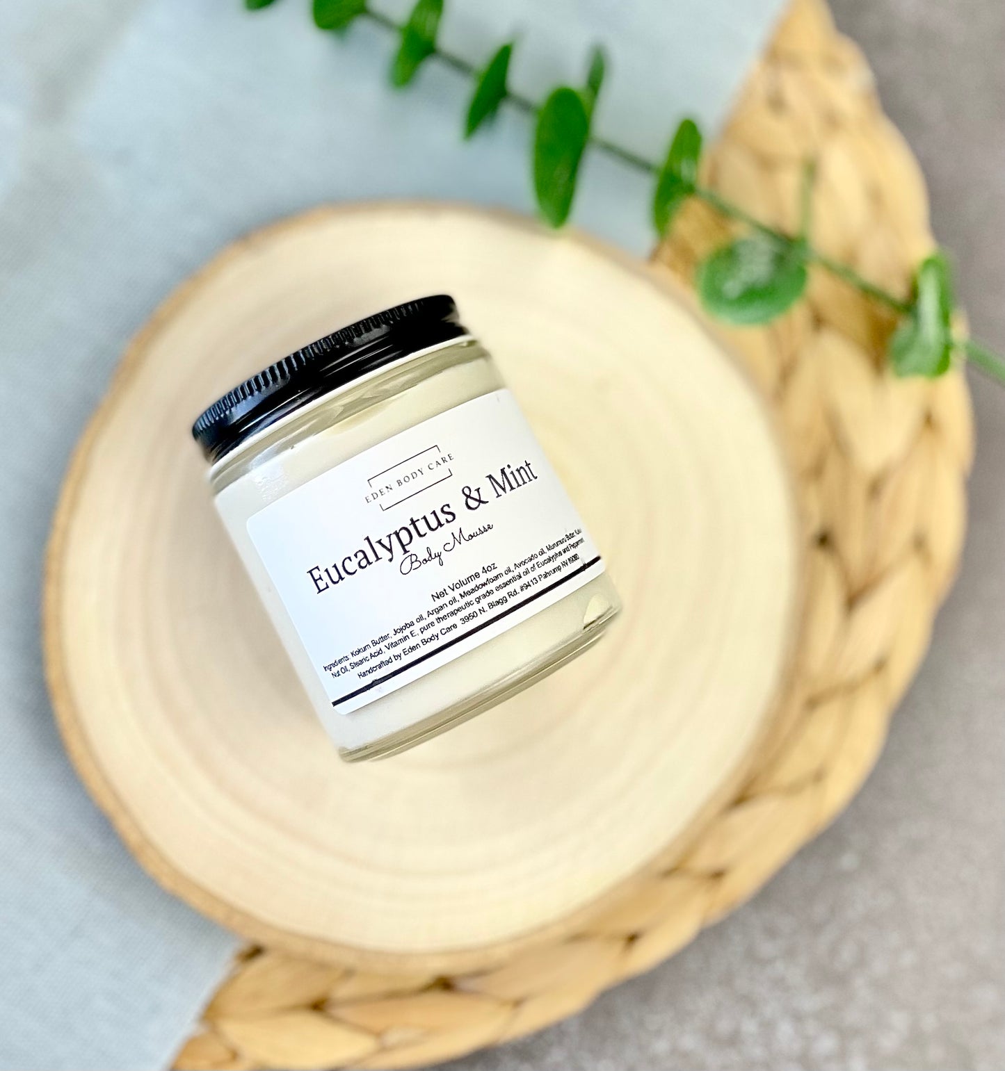 Eden Body Care Eucalyptus & Mint body mousse in a glass jar displayed on a natural wood slice with greenery