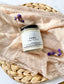 Eden Body Care Fiora whipped body mousse in a glass jar displayed on soft neutral fabric with small purple flowers.
