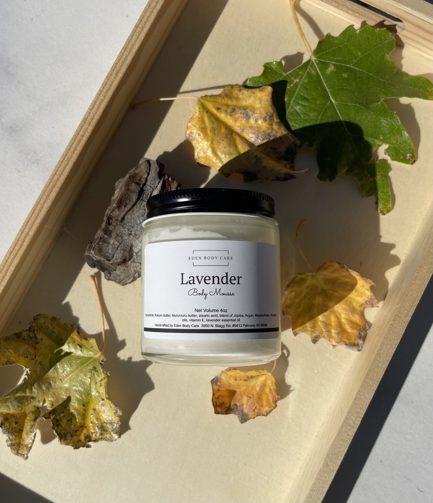Eden Body Care Lavender body mousse jar styled on a white towel in natural sunlight with green leaves around it