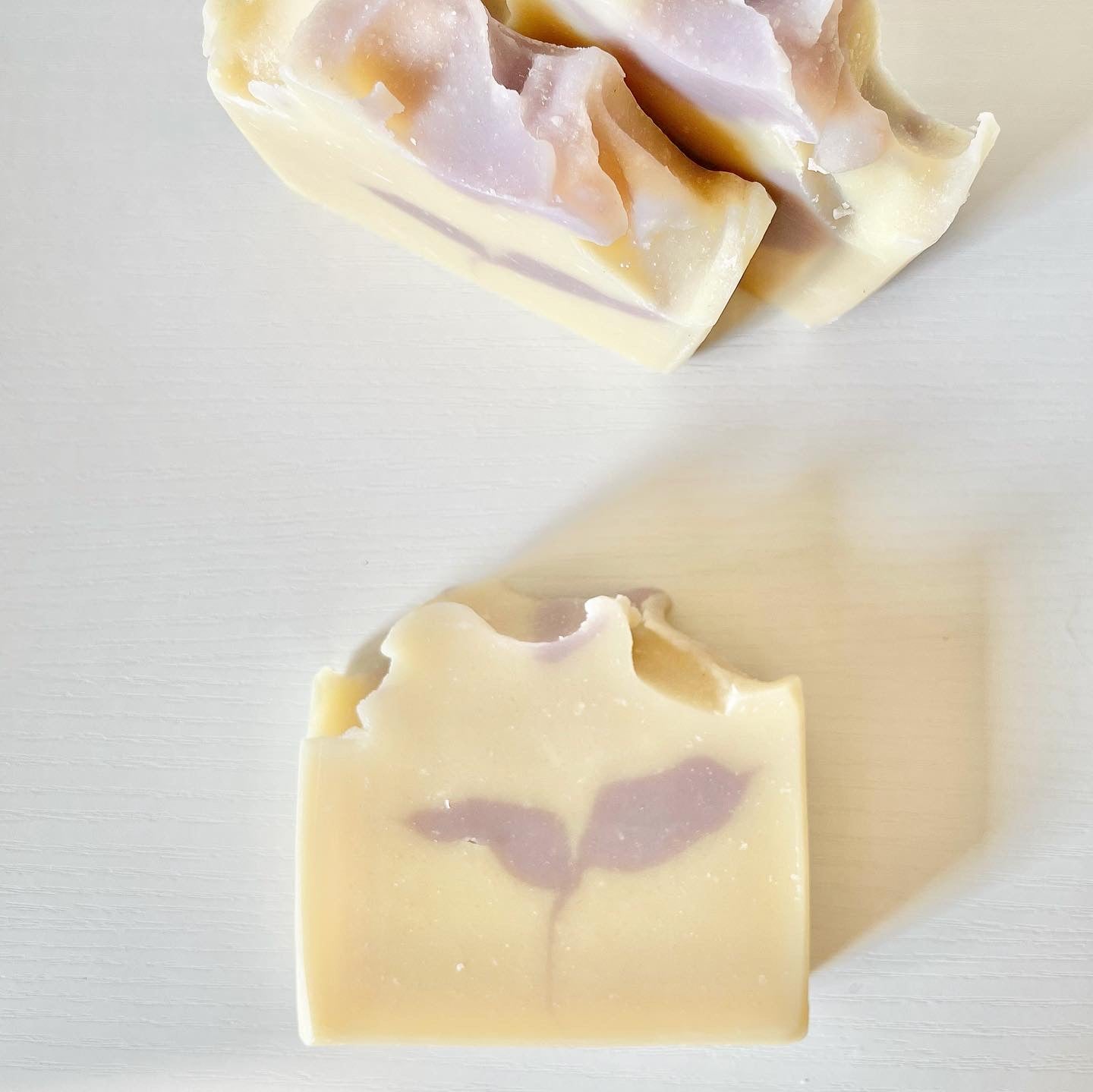 Handmade goat milk soap bars with soft lavender-colored botanical swirls and sculpted tops displayed on a white surface.
