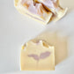 Handmade goat milk soap bars with soft lavender-colored botanical swirls and sculpted tops displayed on a white surface.