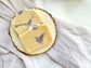 Two handmade goat milk soap bars with soft purple swirls displayed on a natural wood slice over neutral fabric.