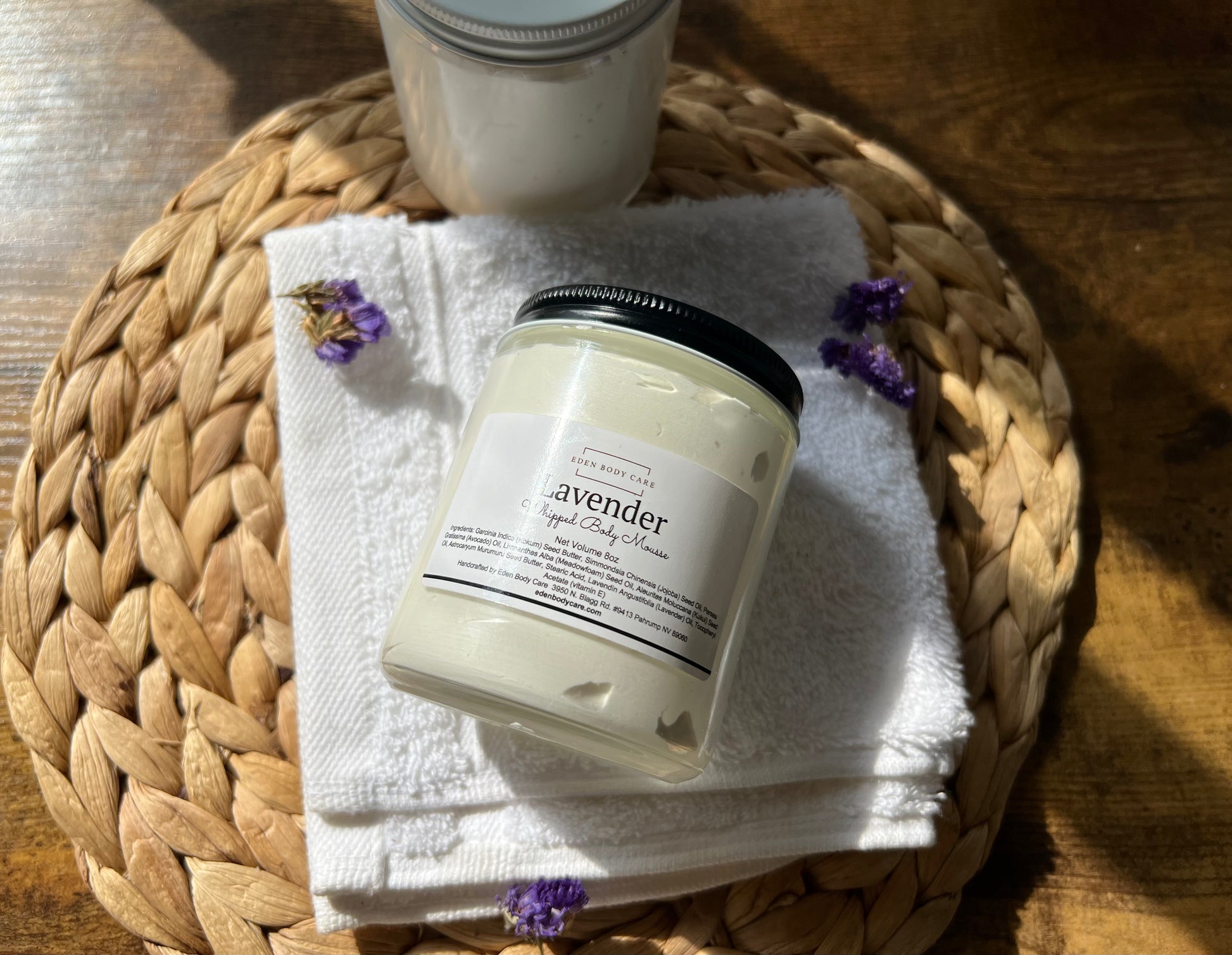 Eden Body Care Lavender whipped body cream jar displayed on a folded white towel with dried purple flowers in warm natural sunlight.