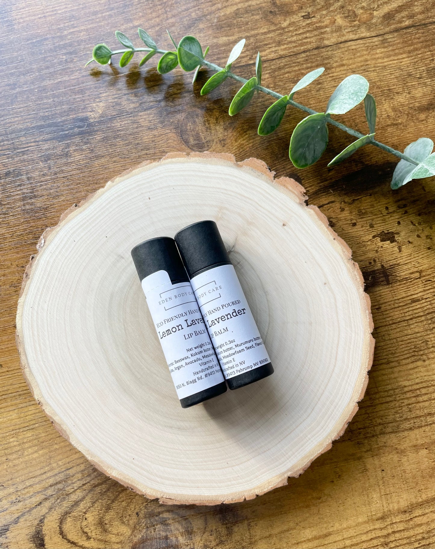 Two Eden Body Care lip balm tubes, Lemon Lavender and Lavender, displayed on a natural wood slice