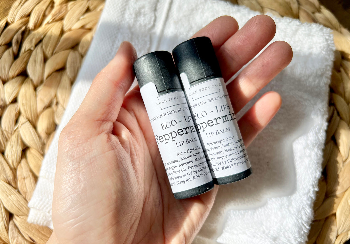 Two Eden Body Care Eco-Lips peppermint lip balm tubes held in hand against a soft  white washcloth background.
