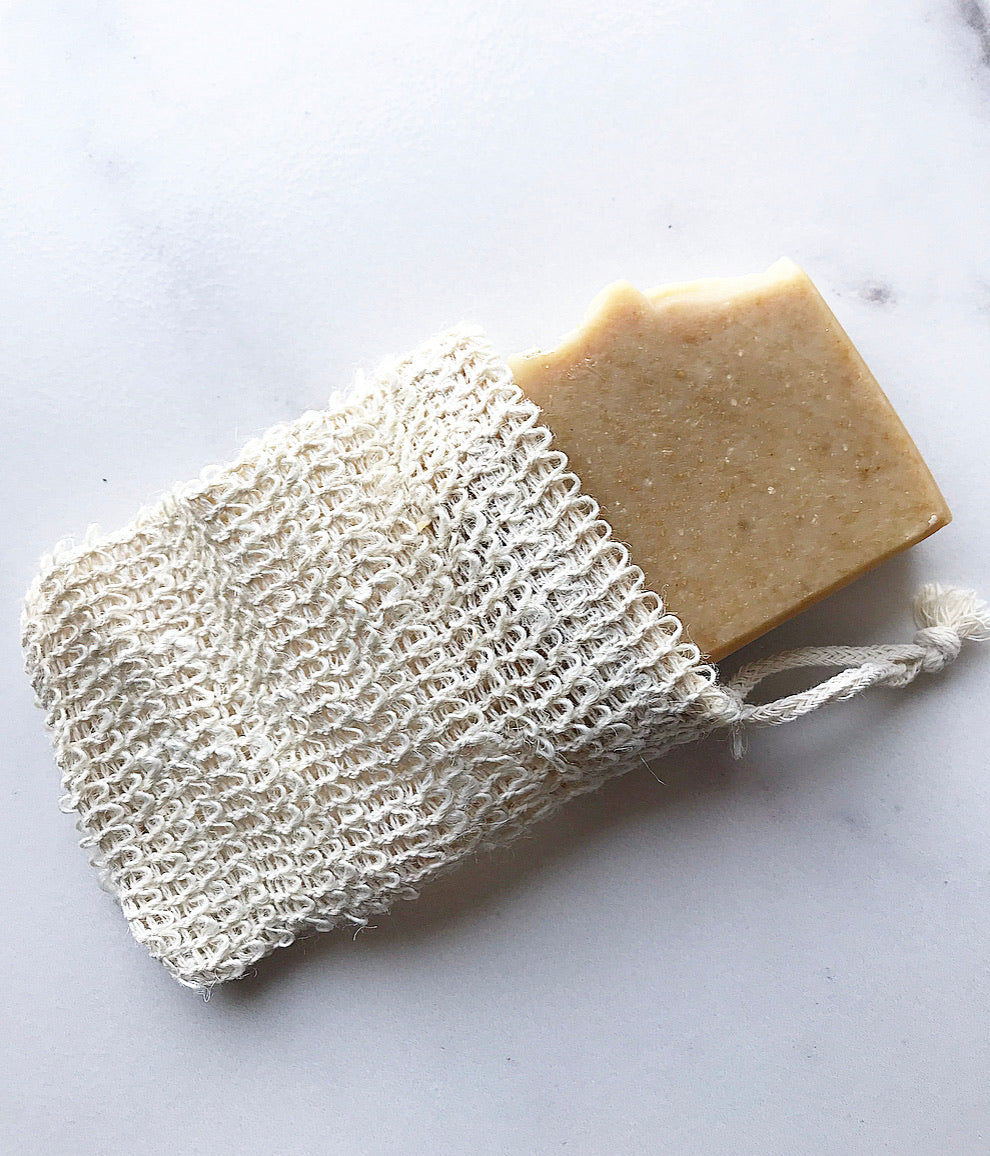 Handmade soap bar partially tucked inside a natural sisal soap saver bag with drawstring closure.