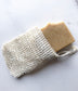 Handmade soap bar partially tucked inside a natural sisal soap saver bag with drawstring closure.