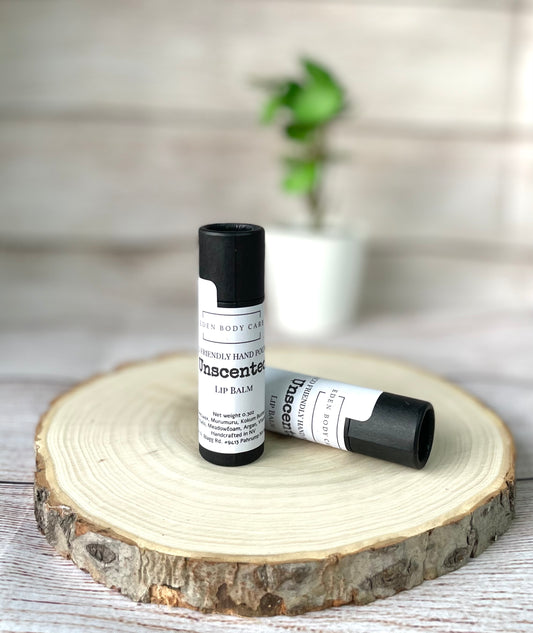 Two Eden Body Care unscented lip balm tubes displayed on a natural wood slice.